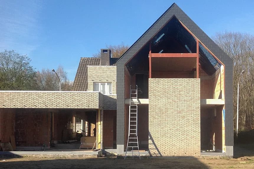 Dakwerken De Haes voert een dakrenovatie uit op een woning in Onze-Lieve-Vrouw-Waver, Heiken: vooraanzicht van de woning in aanbouw met steigerschragen