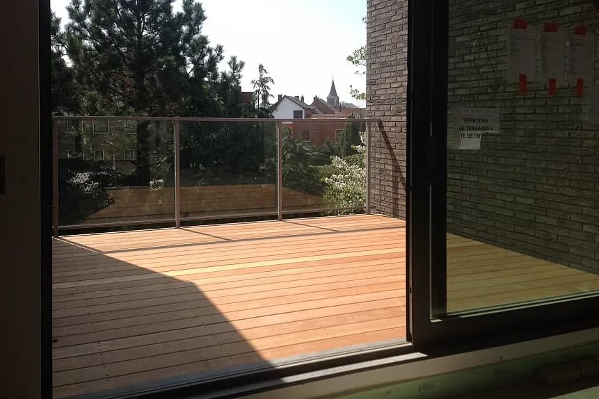 Houten terras met glazen balustrade en zicht op de omgeving, afgewerkt door Dakwerken De Haes in Tremelo, Pharma Finance.